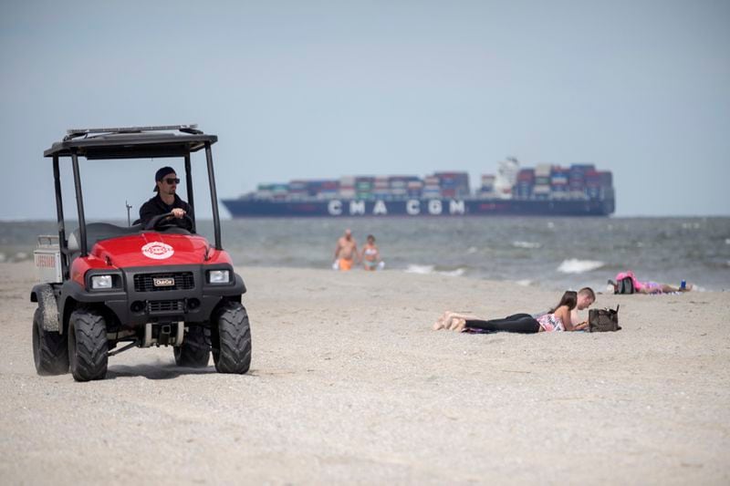 A member of the Tybee Island Life Guards patrols the beach on a ATV while visitors sunbathe in the sand on Saturday, April 4, 2020. (Photo: Stephen B. Morton/Special to the AJC)