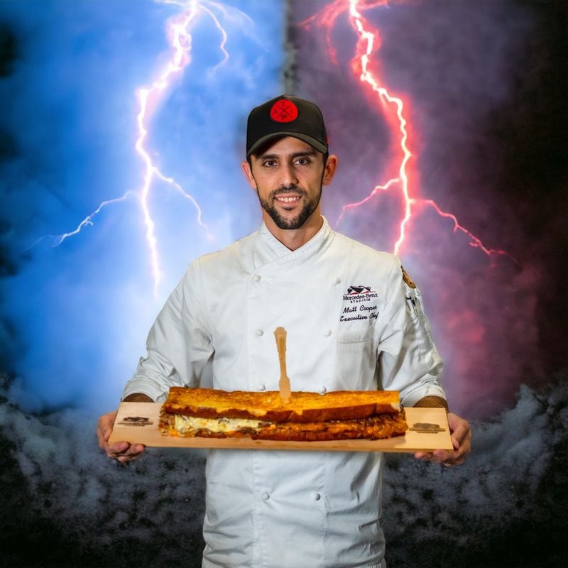 Matt Cooper, senior executive chef at Levy Restaurants, stands with the two-foot-long “dueling” grilled cheese ($25) that will be served during the 2023 SEC Championship Game.