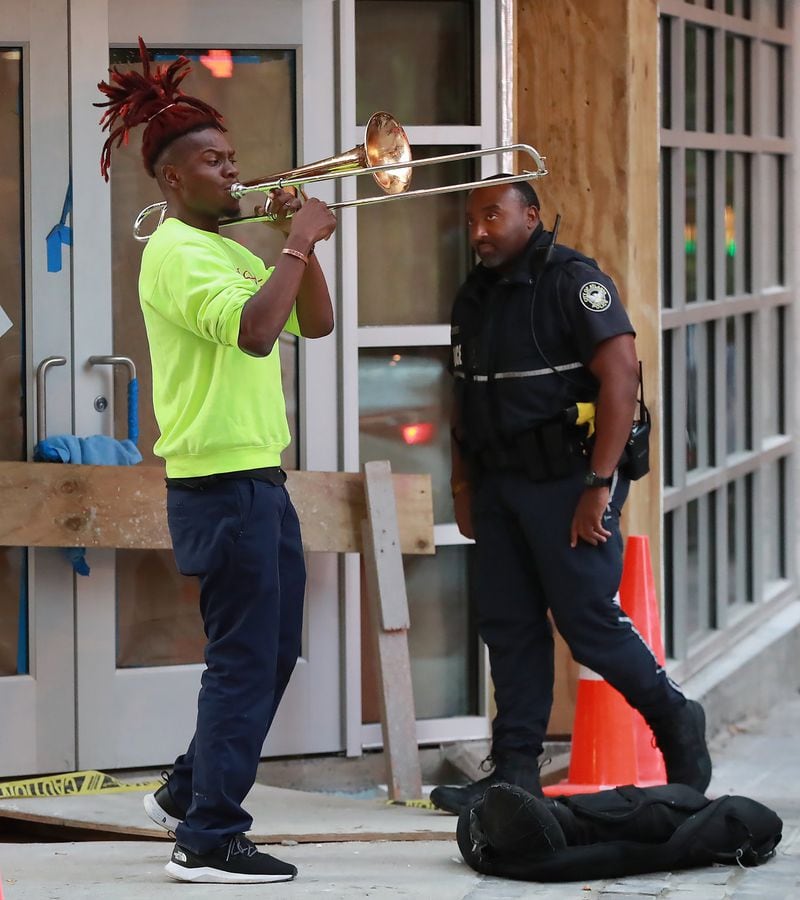 October 16, 2019 Atlanta: An Atlanta police officer looks over street performer Eryk D. Radical, 26, a legally blind Georgia State University student, as he plays his trombone for pedestrians at Peachtree Street and Andrew Young International Boulevard. Radical is suing Atlanta police, MARTA police and the Fulton County Sheriff’s office alleging repeated harassment while playing on street corners. Curtis Compton/ccompton@ajc.com