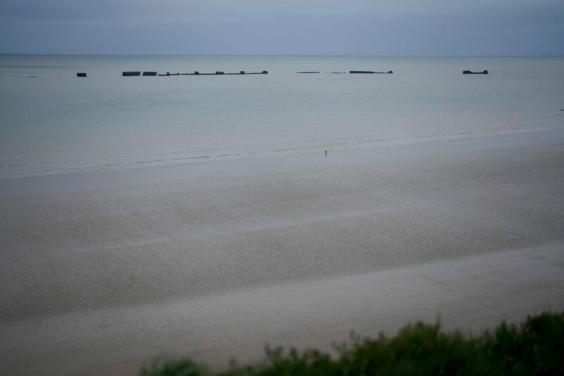 A man walks on Gold beach in Arromanches, Normandy, Wednesday, April 10, 2024. In the background are the remains of the artificial harbor of Arromanches. On D-Day, Charles Shay was a 19-year-old Native American army medic who was ready to give his life — and actually saved many. Now 99, he's spreading a message of peace with tireless dedication as he's about to take part in the 80th celebrations of the landings in Normandy that led to the liberation of France and Europe from Nazi Germany occupation. (AP Photo/Thibault Camus)
