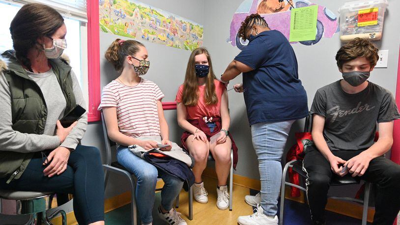 In this file photo from May, Margaret Bell, 14, receives a first dose of the Pfizer-BioNTech vaccine from Melissa Dalton, RMA, as her mother Jessica Bell (left), sister Mary Frances Bell, 12, and brother Griffin Bell (right), 17, look on at Dekalb Pediatric Center. (Hyosub Shin / Hyosub.Shin@ajc.com)