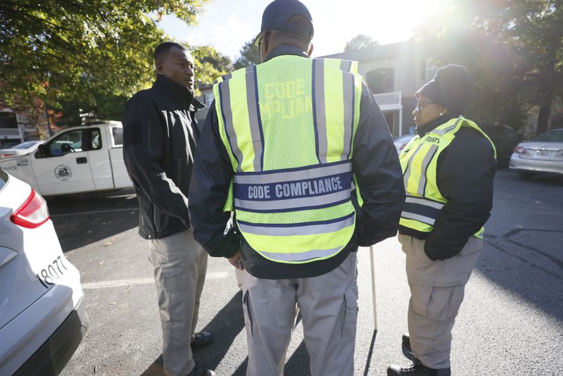 DeKalb County code compliance officers huddle in the parking lot of Woodside Village Apartments near Clarkston before an October inspections sweep. In these sweeps, officers cite exterior conditions that violate county ordinances. (Miguel Martinez / miguel.martinezjimenez@ajc.com)