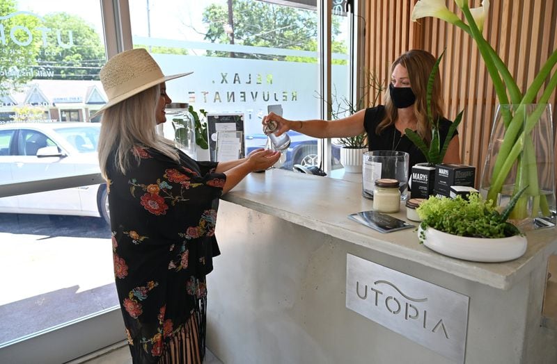 Julie Stewart, owner, offers hand sanitizer to customer Katie Cooper at Utopia Foot & Shoulder Massage in Atlanta on Thursday, June 11, 2020. PHOTO: Hyosub Shin/Hyosub.Shin@ajc.com)