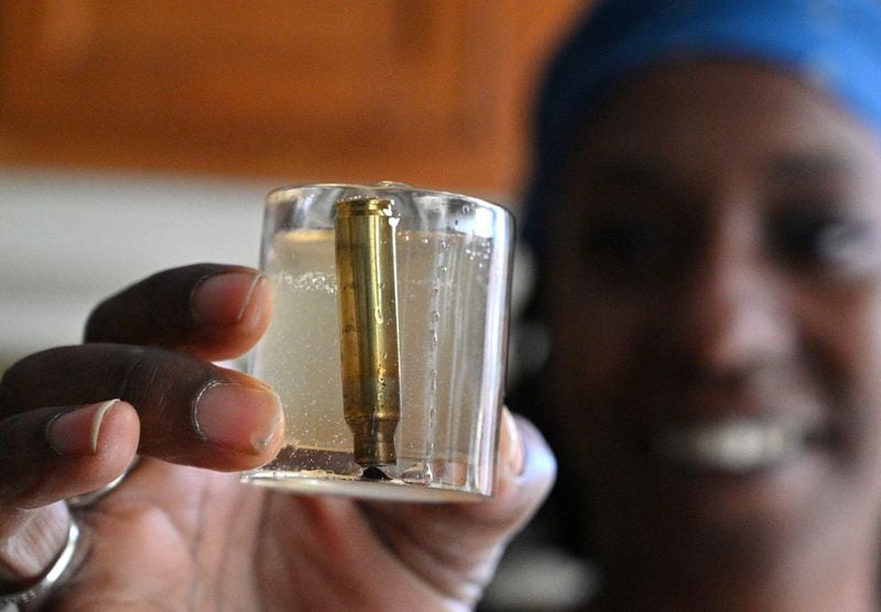Danielle Russell shows in December 2021 one of the shot glasses that she made with the dozens of empty bullet cartridges that she found on walks to her mailbox at Atlanta's Pavilion Place. She has made about two dozen of these glasses so far. (Hyosub Shin/Hyosub.Shin@ajc.com)