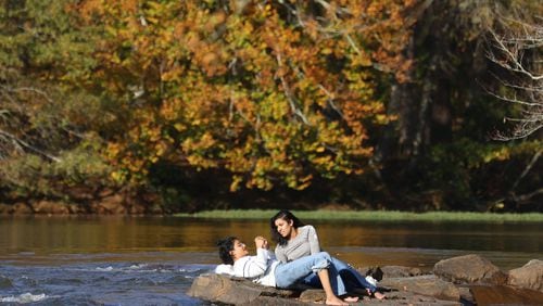 Two girls sit by the waters edge on the Chattahoochee River as fall foliage is shown at Jones Bridge Park, Thursday, November 3, 2022, in Peachtree Corners, Ga. (Jason Getz / Jason.Getz@ajc.com)