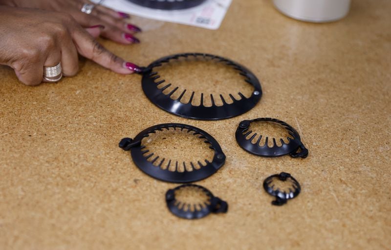 Ceata Lash, founder and owner of PuffCuff, points to the different sizes of her product in her office in Marietta on Tuesday, Feb. 20, 2024. The company makes specialized clasps for people with curly hair. (Natrice Miller/ Natrice.miller@ajc.com)