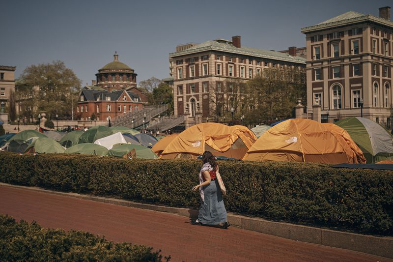 A woman wearing a keffiyeh walks by a pro-Palestinian encampment, advocating for financial disclosure and divestment from all companies tied to Israel and calling for a permanent cease-fire in Gaza, inside Columbia University Campus on Sunday, April 28, 2024, in New York. (AP Photo/Andres Kudacki)