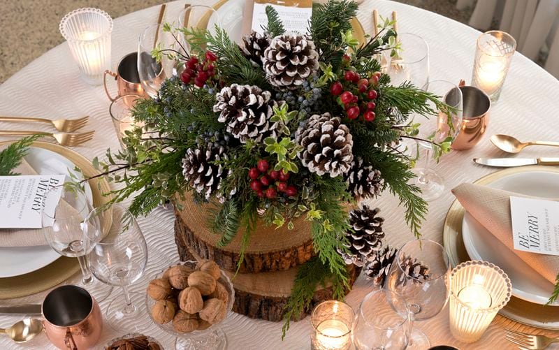 The centerpiece on this table, from BBJ Linen, creates a rustic yet elegant ambiance. A tree log base tapped with frosted pine cones and pine accents contrast with traditional fine china and glassware.
