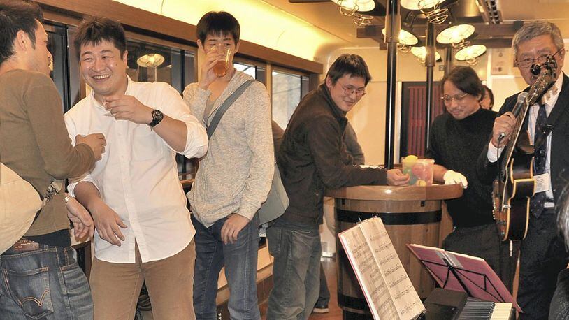 Reporter Masanori Matsumoto, second from left, samples the sake while listening to a live jazz performance on the Koshino Shu Kura train. The table is designed to resemble a sake barrel. PHOTO: Japan News-Yomiuri