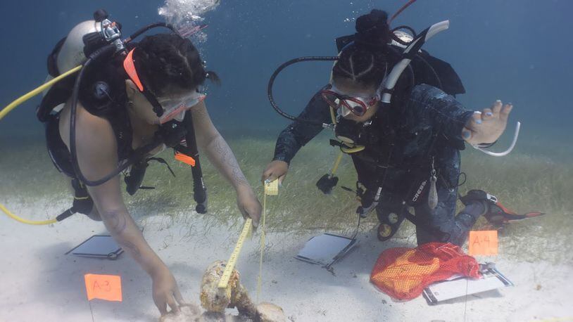 Jasmine Mariaca and Skye Garrette measure an artifact from the remains of an 18th-century wreck located inside Biscayne National Park. Divers use tape measures, folding ruler, pencils, and mylar paper to take and record accurate measurements. The collected data is later recorded onto a "site map" which will be stored for history. (Chris G Searles / Used with permission)