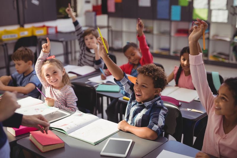 Schoolkids raising their hands in classroom at school