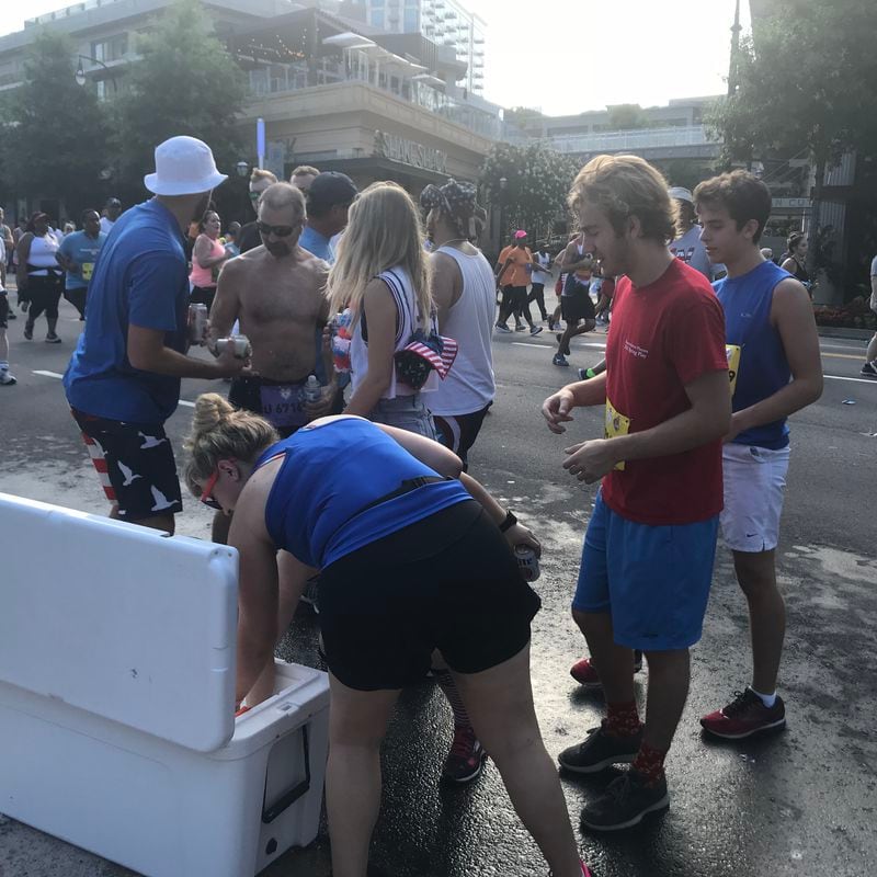 Spectators hand out dozens of beers to AJC Peachtree Road Race runners. “If you ain’t drinking, you ain’t trying,” one of the men explains.