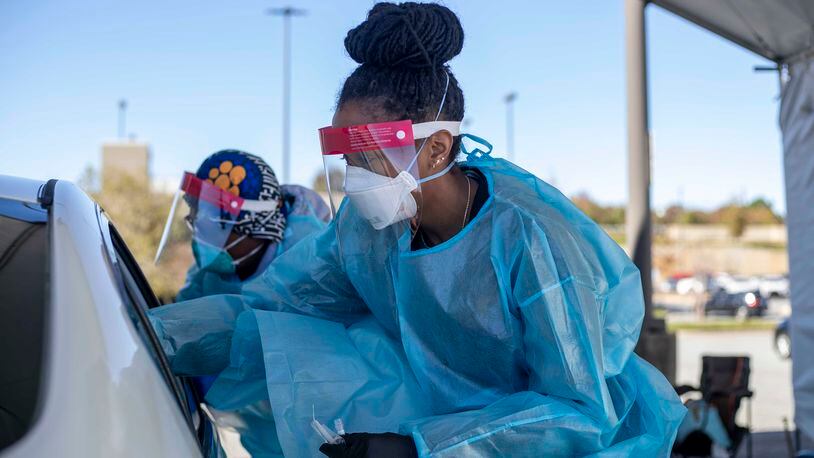 11/17/2020 -  Atlanta, Georgia - Two nurses work around a car with four individuals receiving COVID-19 tests at a DeKalb County Department of Health COVID-19 drive-thru testing site in Atlanta, Tuesday, November 17, 2020.  (Alyssa Pointer / Atlanta Journal-Constitution)