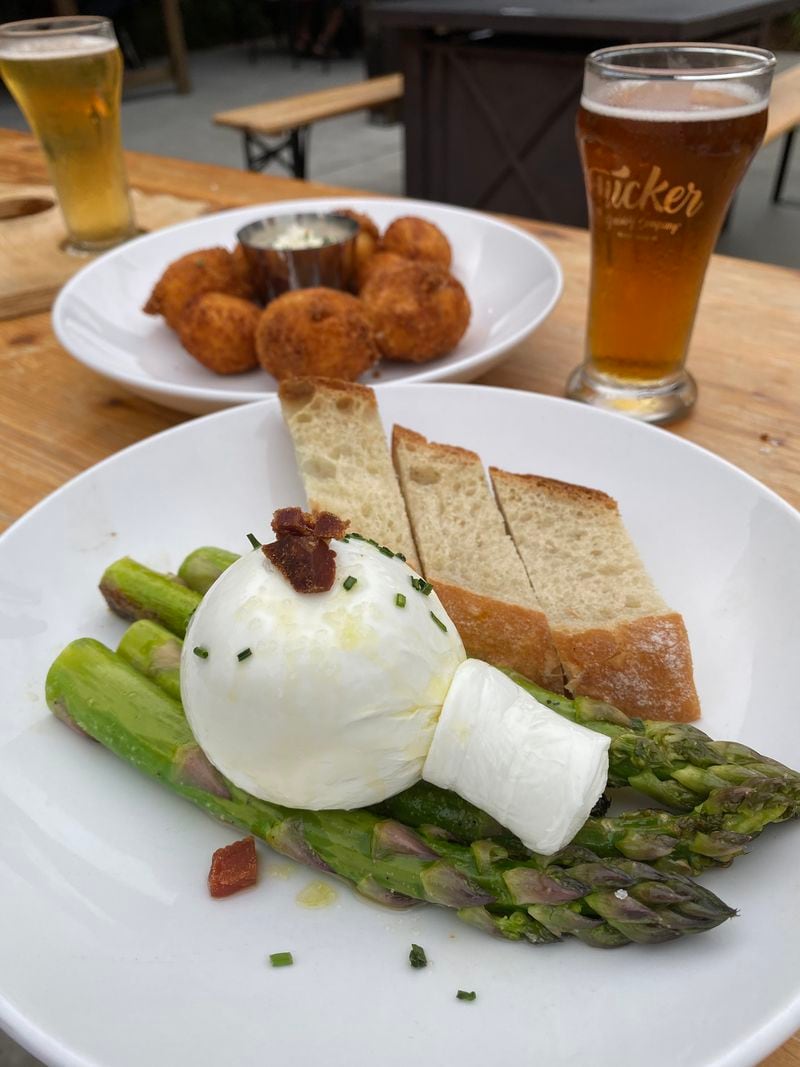 Seared jumbo asparagus with house-made burrata (foreground) and sauerkraut bites are two shareable plates on the Tucker Brewing menu. Ligaya Figueras/ligaya.figueras@ajc.com