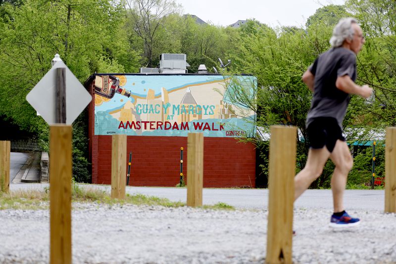A person jogs by the Beltline across from Amsterdam Walk shopping center on Tuesday, April 4, 2023.  Portman Holdings is pursuing a plan to redevelop Amsterdam Walk, a 9-acre shopping center along the Beltline and Piedmont Park.   Miguel Martinez / miguel.martinezjimenez@ajc.com