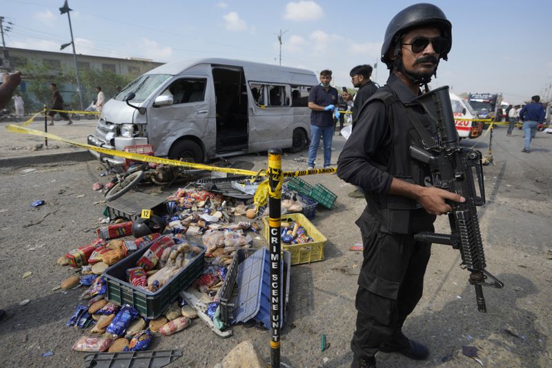 A Pakistani police officer stands guard as investigators examine the scene of a suicide attack in Karachi, Pakistan, Friday, April 19, 2024. A suicide bomber detonated his explosive-laden vest near a van carrying Japanese autoworkers, who narrowly escaped the attack Friday that wounded some bystanders in Pakistan's port city of Karachi, police said.(AP Photo/Fareed Khan)
