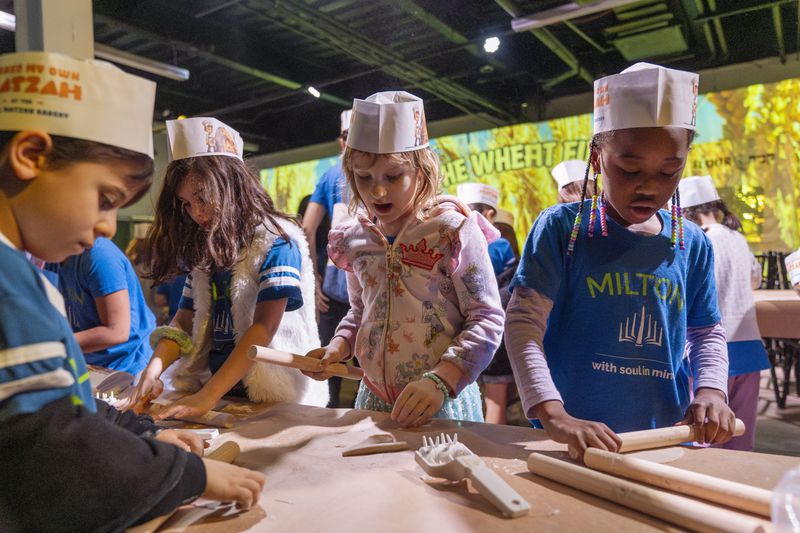 Hana Chmeruk, center, who moved to the U.S. from Ukraine, and Avigael Yahyisrael, 7, make matzah with other first graders from Milton Gottesman Jewish Day School of the Nation's Capitol, during a "Matzah Factory" field trip to the JCrafts Center for Jewish Life and Tradition in Rockville, Md., Thursday, April 18, 2024, ahead of the Passover holiday which begins next Monday evening. To be kosher for Passover the dough has to be prepared and cooked all within 18 minutes and not allowed to rise. (AP Photo/Jacquelyn Martin)