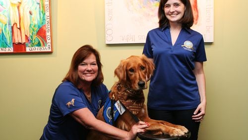 Luke, the comfort dog, and two of his handlers — Judy Adams (left, kneeling) and Michelle Malaski (standing). David Ibata for the AJC