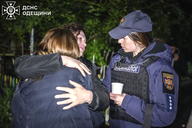 In this photo provided by the Ukrainian Emergency Service, emergency service psychologist, right, comforts women at the scene of a building that was damaged by night Russian drone attack in Odesa, Ukraine, Tuesday, April 23, 2024. (Ukrainian Emergency Service via AP)