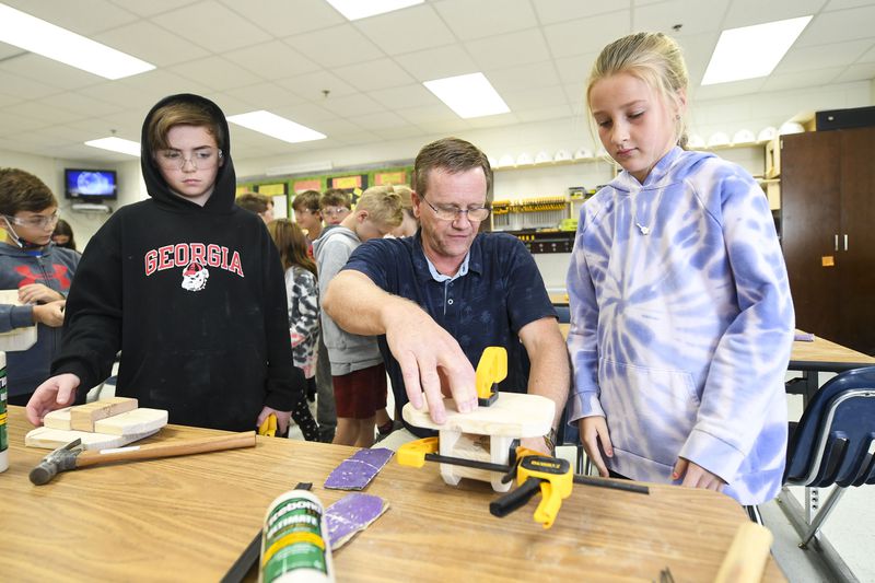 Fourth grade students Luke Wilson, 10 (left), and Madison Watford, 9, look on as instructor Scott Selvig (center) demonstrates how to clamp boards at Mountain Park Elementary School on Nov. 10, 2021. (Daniel Varnado/ For the Atlanta Journal-Constitution)