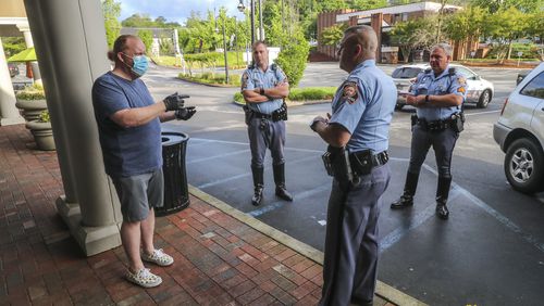 Barber and owner of Chris Edwards wears a mask (left) as he talks with GSP Troopers who were responding to a complaint call that there was a crowd gathering at the shop at Peachtree Battle Barber Shop at 2333 Peachtree Road in Atlanta on Friday, April 24, 2020. The Troopers found the business in compliance.