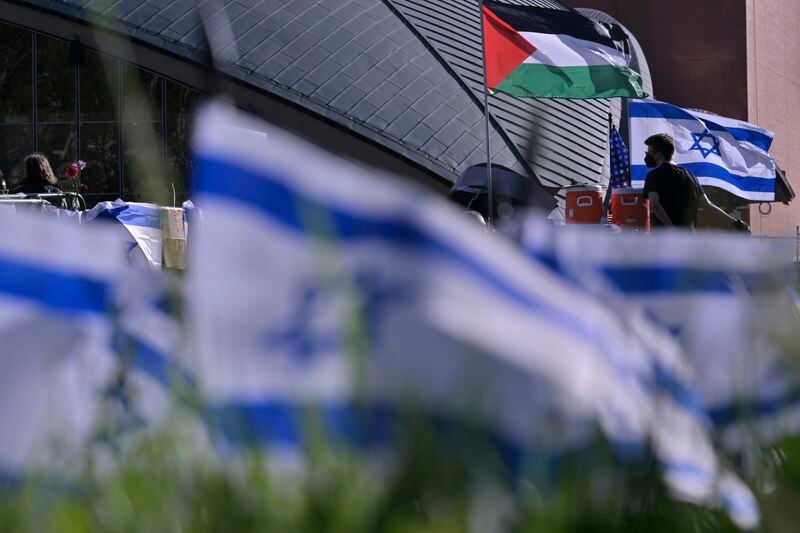 A man walks below flags at a Pro-Palestinian encampment at MIT, Thursday, May 9, 2024, in Cambridge, Mass. MIT has suspended 23 students for participating in the encampment, and police detained at least three during a demonstration at the nearby Stata center, where demonstrators blocked traffic over claims the university was conducting research which would be used for Israeli military drones. (AP Photo/Josh Reynolds)