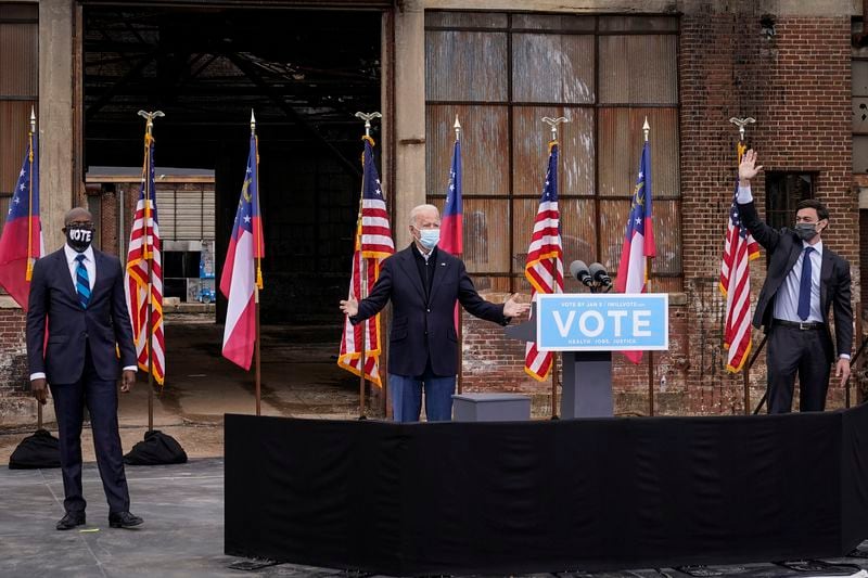 Flanked by Democratic U.S. Senate candidates Rev. Raphael Warnock, left, and Jon Ossoff, U.S. President-elect Joe Biden gestures to the crowd at the end of a drive-in rally at Pullman Yard on December 15, 2020 in Atlanta, Georgia. (Drew Angerer/Getty Images/TNS)