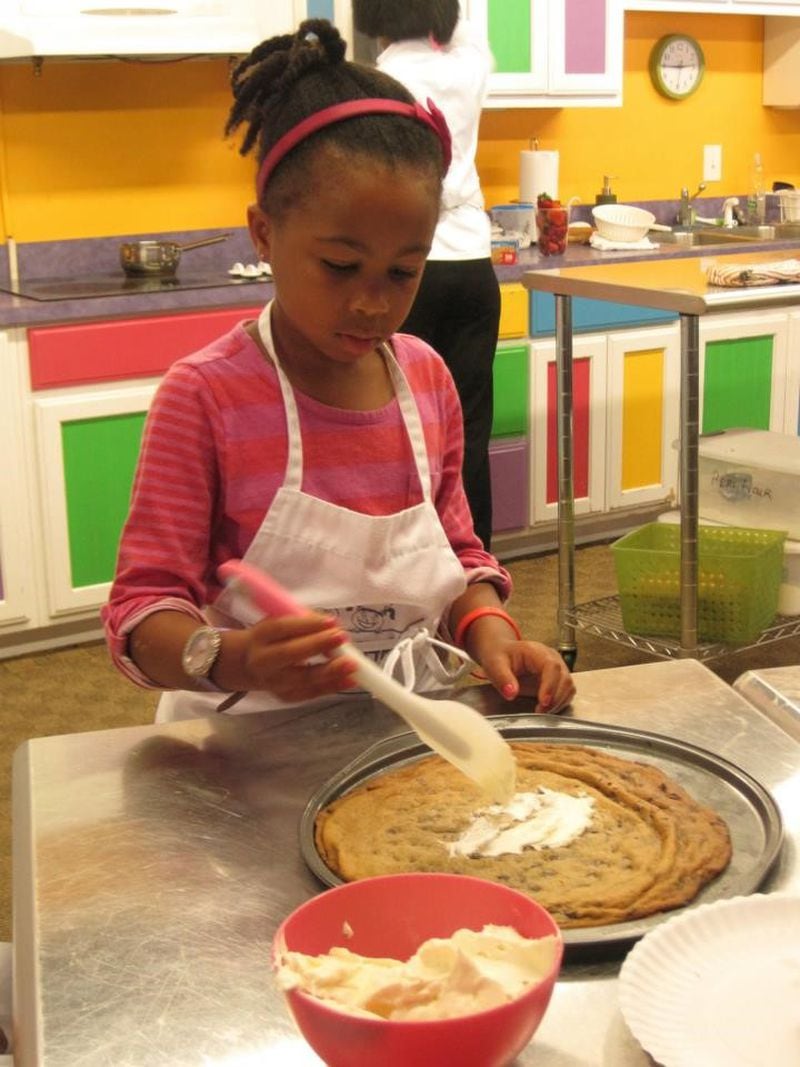 In this file photo, a budding kid chef at Young Chefs Academy in Atlanta concentrates on icing a large chocolate chip cookie she baked in the brightly colored kitchen.
