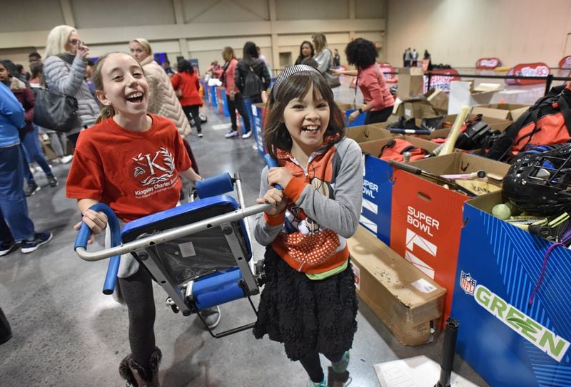 Emily Friedenberg (left), 10, and Millyn Chan, 9, bring in their donation during the NFL’s Super Kids-Super Sharing project at the Infinite Energy Forum in Duluth. HYOSUB SHIN / HSHIN@AJC.COM