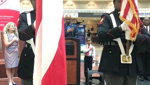 During the national anthem at a Hartsfield-Jackson Independence Day event on June 28, 2018, Simon Noellin, 5, is flanked by USO Georgia CEO Mary Lou Austin, left, Hartsfield-Jackson customer experience director Steve Mayers at the podium, and assistant general manager Richard Duncan, right.