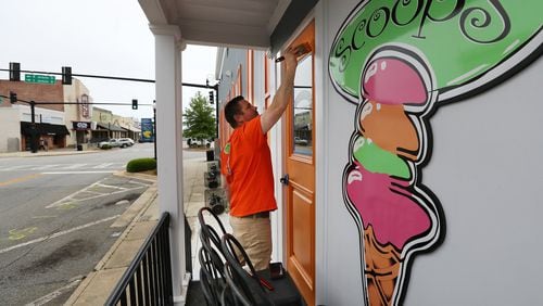 Brian Lambert paints a door as he gets ready to reopen Scoops, the ice cream shop he and his wife, Christie, own in Forsyth. They plan to take advantage of Gov. Brian Kemp’s order to allow some of the state’s businesses to reopen Friday after they have been shuttered in the midst of the coronavirus pandemic. “We have to open our doors, or our business will go under,” Christie Lambert said. Curtis Compton ccompton@ajc.com