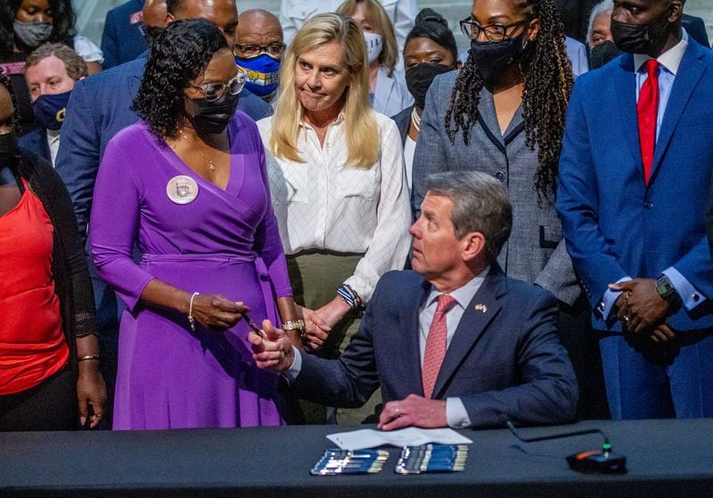 Gov. Brian Kemp hands Wanda Cooper-Jones (left) a pen as first lady Marty Kemp watches after Kemp signed HB 479, which repeals Georgia's citizen's arrest law at the State Capitol on May 10, 2021.   (STEVE SCHAEFER for the Atlanta Journal-Constitution)