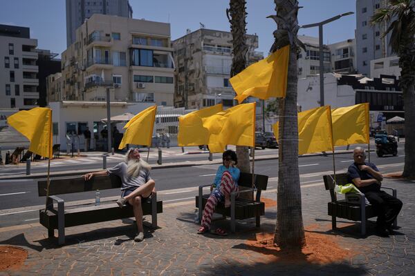 People sit on benches, decorated with yellow flags symbolizing the hostages being held by Hamas in the Gaza Strip, at the beachfront in Tel Aviv, Israel, Friday, July 4, 2025. (AP Photo/Oded Balilty)