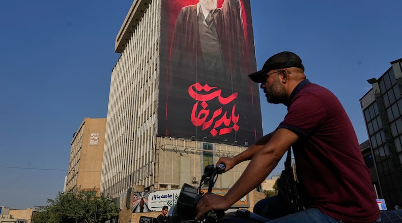A man rides on his motorbike past a billboard with a message that reads in Farsi: " We must rise up" and an image of the late Iranian Supreme Leader Ayatollah Ali Khamenei, who was killed during the U.S. and Israel strikes on Feb. 28, in Tehran, Iran, Saturday, Aug. 15, 2026. (AP Photo/Vahid Salemi)