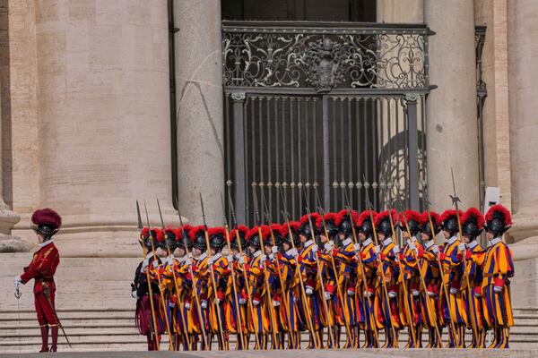Pontifical Swiss guards stand in formation in St. Peter's Square as people await the arrival of the body of Pope Francis, who will lie in state at St. Peter's Basilica for three days, at the Vatican, Wednesday, April 23, 2025. (AP Photo/Bernat Armangue)