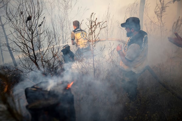 Emergency responders with the Syrian Civil Defense, known as the White Helmets, work to extinguish a wildfire near the town of Rabia, in Syria's Latakia countryside, Sunday, July 6, 2025. (AP Photo/Ghaith Alsayed)