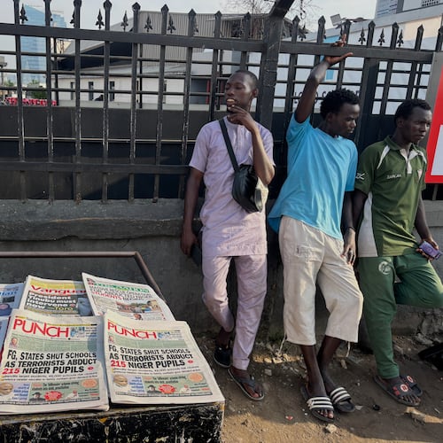 People stand near a display local newspapers on the street of Lagos with headlines on gunmen abducting schoolchildren and staff of the St. Mary's Catholic Primary and Secondary School in Papiri community in Nigeria, Saturday, Nov. 22, 2025. (AP Photo/Sunday Alamba )