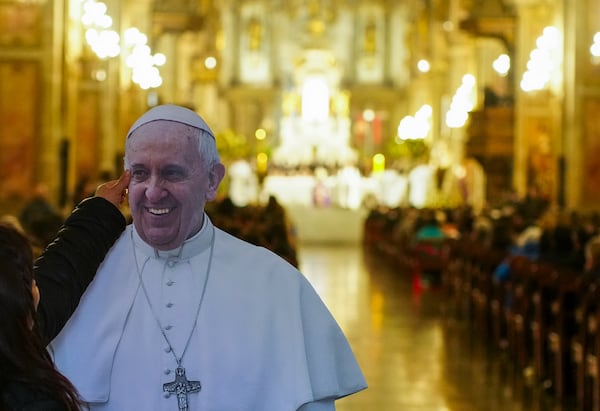 A woman reaches up to touch a life-size cutout of Pope Francis ahead of a Requiem Mass at the Cathedral in Santiago, Chile, Saturday, April 26, 2025. (AP Photo/Esteban Felix)