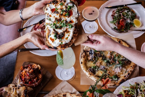 Overhead shot of a table full of Italian food, with a pair of hands passing a flatbread across the table to another waiting hand.