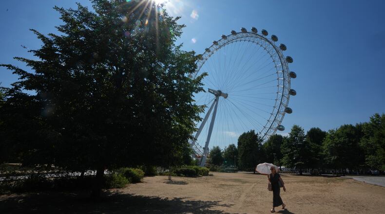 A woman shades under an umbrella as she walks past the London Eye during the fifth heatwave of the year in London, Thursday, Aug. 13, 2026. (AP Photo/Kirsty Wigglesworth)