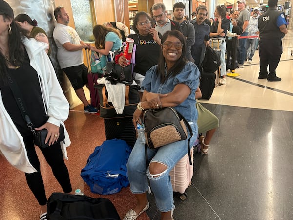 Atlanta airport passenger Troy Lawrence sits on her suitcase Sunday as she waits in the hourslong security line that snaked through the north terminal. Lawrence said she was trying to make back to Omaha, Nebraska to open her childcare facility in the morning.  
(Shaddi Abusaid/shaddi.abusaid@ajc.com)