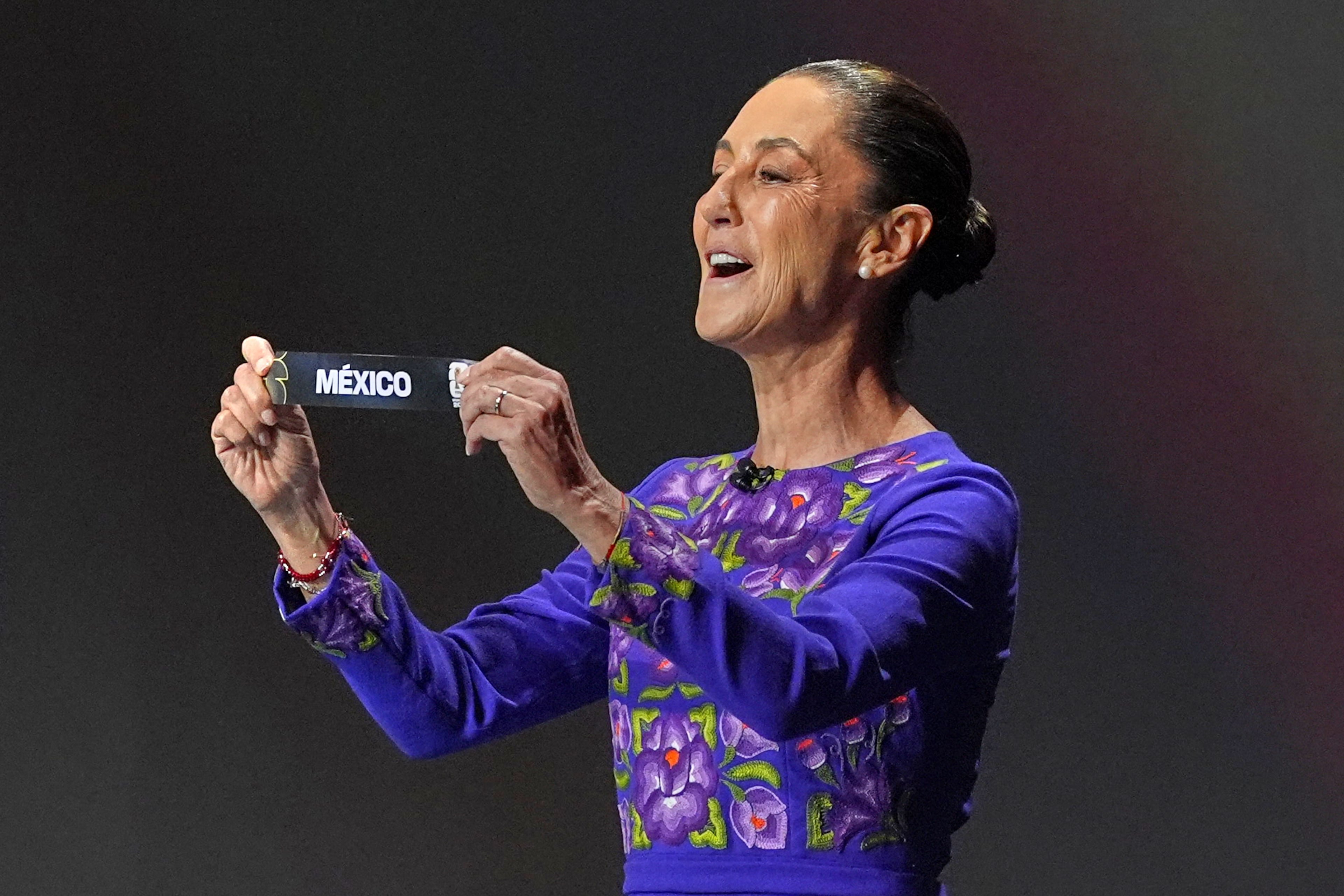 Mexican President Claudia Sheinbaum holds up the team name of Mexico during the draw for the 2026 soccer World Cup at the Kennedy Center in Washington, Friday, Dec. 5, 2025. (AP Photo/Jacquelyn Martin)