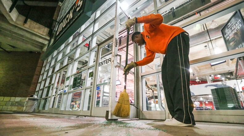 An employee sweeps up glass after a predawn smash-and-grab burglary at Dick’s Sporting Goods in Buckhead. JOHN SPINK / JSPINK@AJC.COM