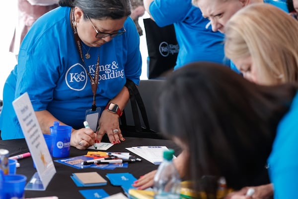Employees write words of encouragement to place inside hygiene kits for people in need. The firm is celebrating its 140th anniversary with 140 community service projects. (Natrice Miller/AJC)