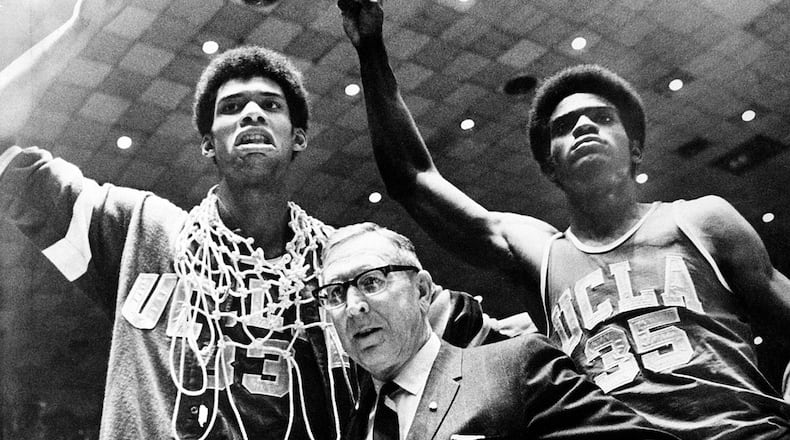 In this March 24, 1969, file photo, UCLA coach John Wooden is flanked by Sidney Wicks, right, and Lew Alcindor, draped with the nets, after the Bruins beat Purdue 92-72 to win the NCAA title for the third consecutive year.