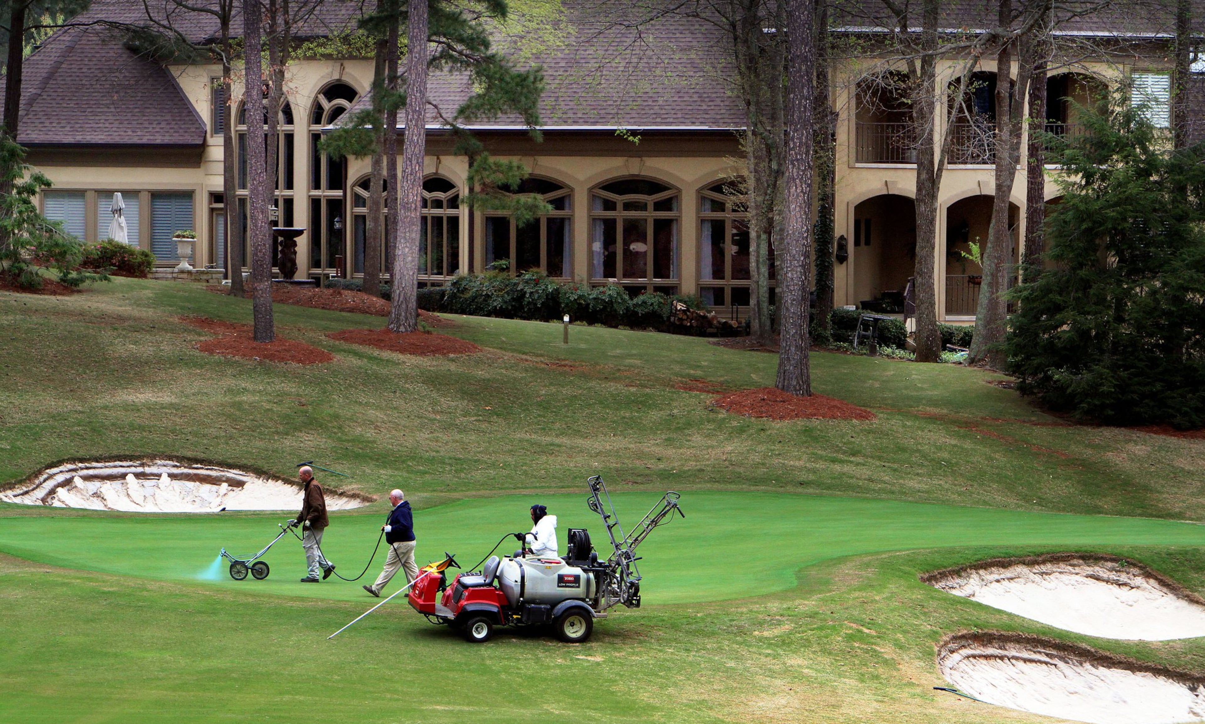 Grounds crews work on a green as a huge home sits nearby on the golf course at the Country Club of the South in Johns Creek. (AJC File)