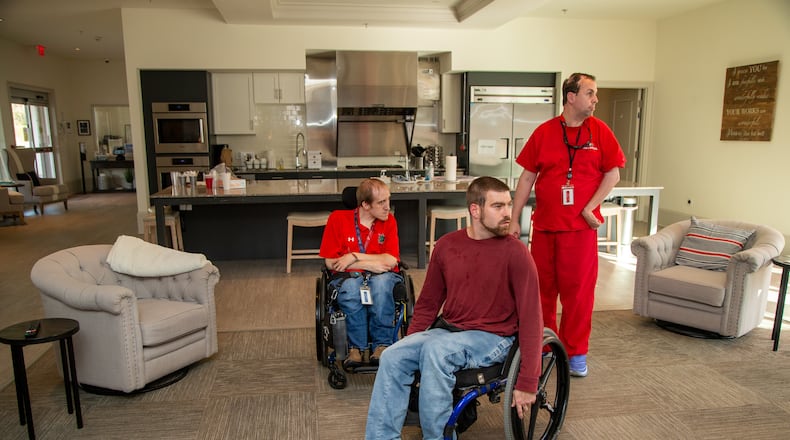 Residents  Adam Laarhoven (from left), Matt Thompson and Ryan Carroll get settled in the main room at Champions Place. The facility is a first-of-a-kind residential community for physically challenged young adults. PHIL SKINNER FOR THE ATLANTA JOURNAL-CONSTITUTION.