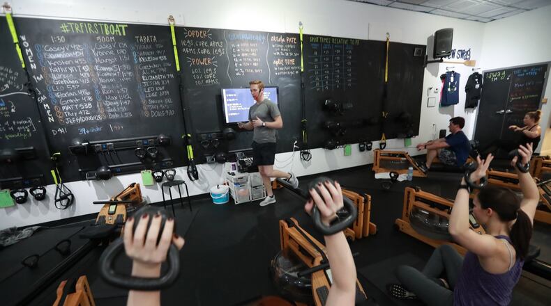 Dylan Loope, a trainer at Total Row Fitness, leads a fitness class on rowing machines in Atlanta. Loope pieces together a living from multiple part-time trainer jobs. Curtis Compton ccompton@ajc.com