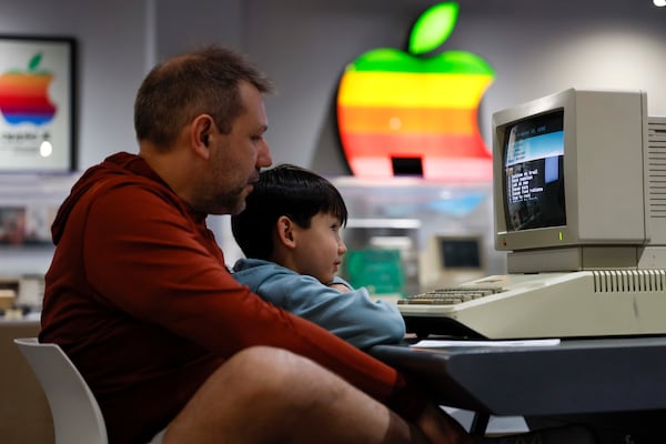 Daniel Marques and his son Theo Marques (7) look at the Oregon Trail video game on a 1985 computer at the Apple exhibit at the Mimms Museum in Roswell. (Miguel Martinez/AJC)