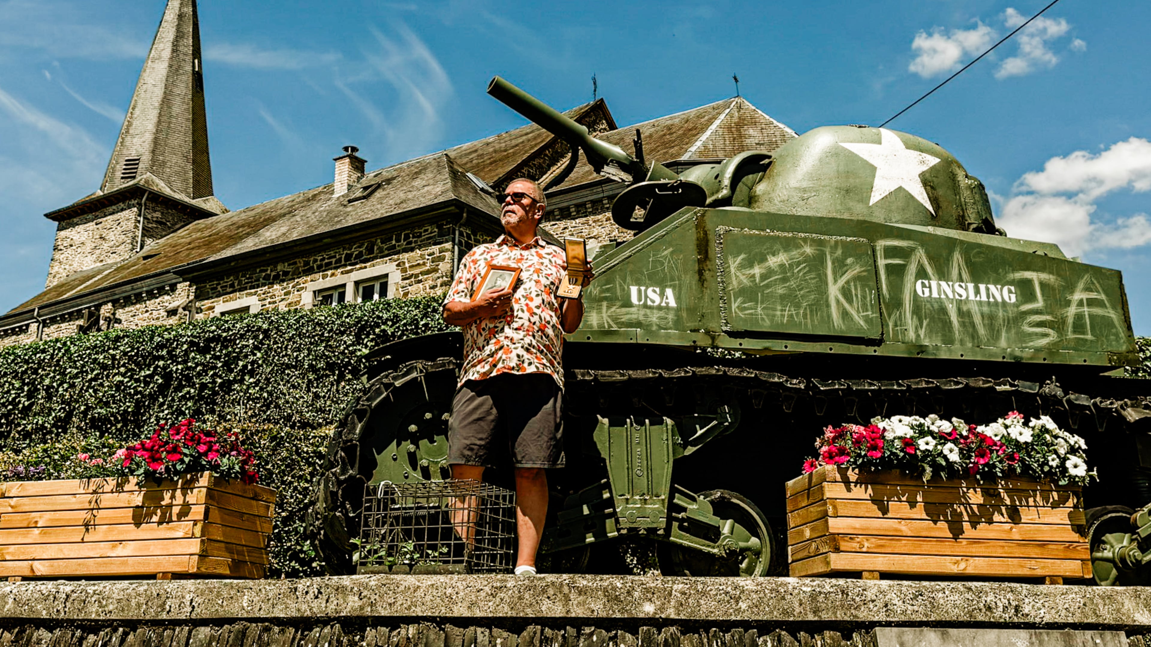 Len Garrison displays his father’s photo and Silver Star in front of a Sherman Tank in Wibrin, Belgium. (Courtesy of Judith Garrison)